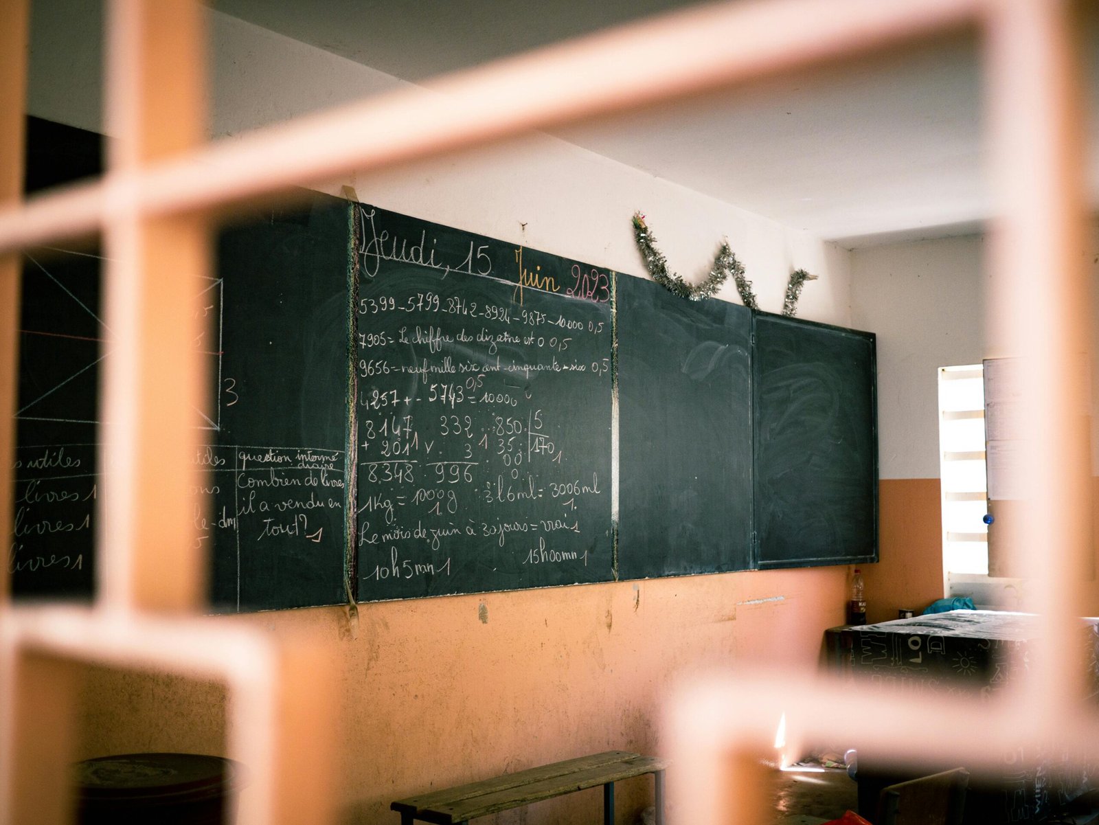 A classroom with a blackboard displaying mathematical equations in French, seen through a window.